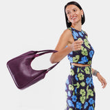Plum Large | A model holding a u-shaped, flat-bottomed leather shoulder bag with two outside pockets