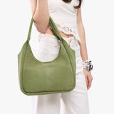 Laurel Medium | A model holding a u-shaped, flat-bottomed leather shoulder bag with two outside pockets
