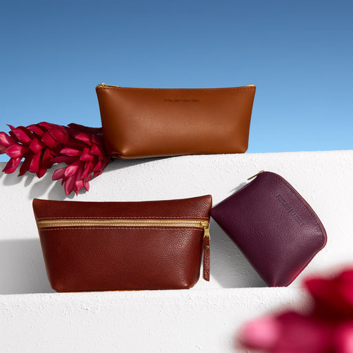 Three leather pouches in brown and maroon with gold zippers on a white surface with pink flowers. featured image