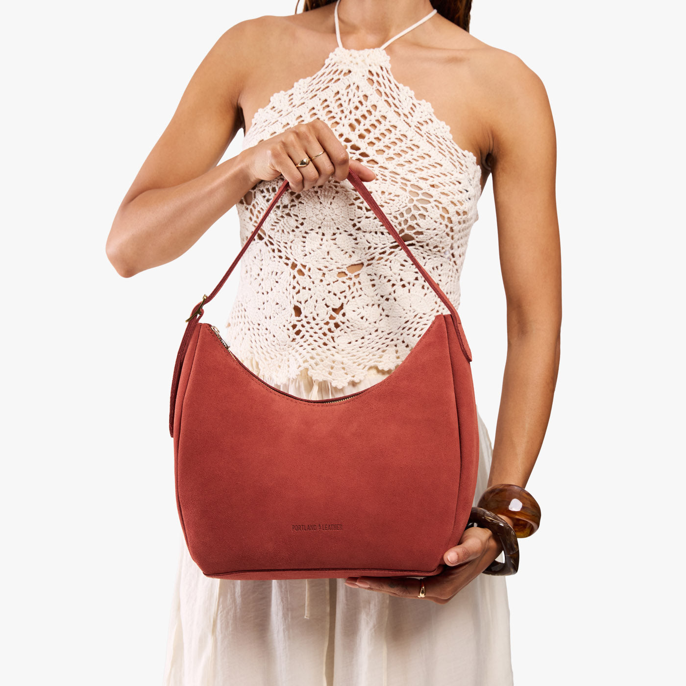 Cinnabar*Medium | Model holding u-shaped, flat-bottomed leather shoulder bag with adjustable strap