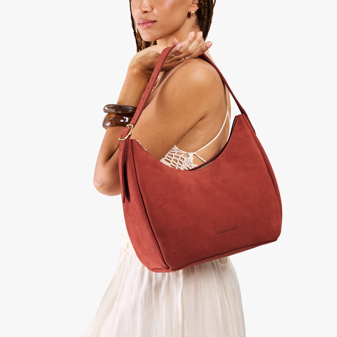 Cinnabar*Medium | Model holding u-shaped, flat-bottomed leather shoulder bag with adjustable strap