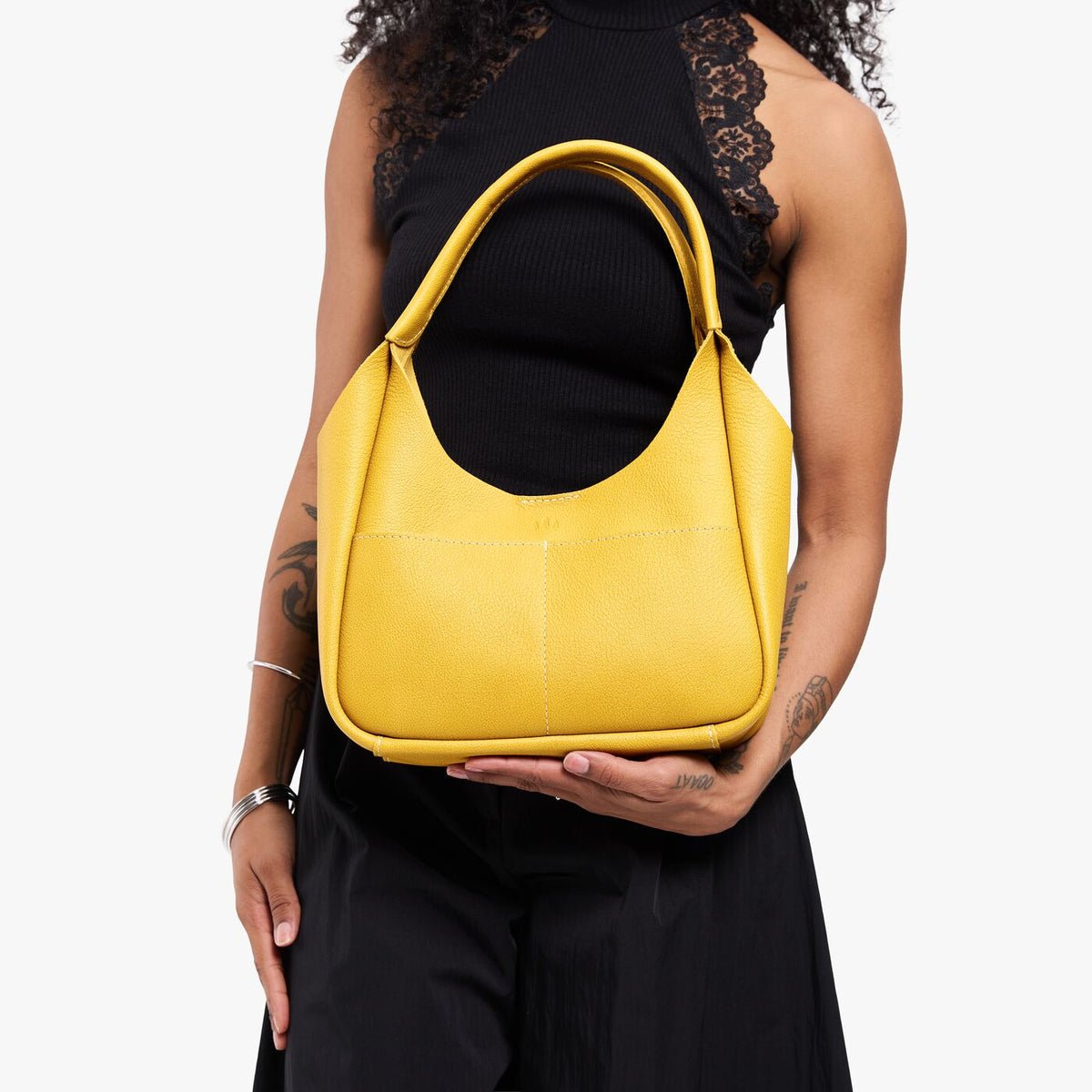 Pomello*Medium | Model holding a u-shaped, flat-bottomed leather shoulder bag with two outside pockets