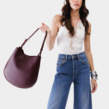 Plum Large | Woman wearing rounded shoulder bag with adjustable strap on a white background