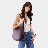 Plum Large | Woman wearing rounded shoulder bag with adjustable strap on a white background