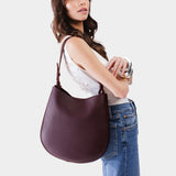 Plum Large | Woman wearing rounded shoulder bag with adjustable strap on a white background
