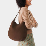 Stagecoach Large | Woman wearing rounded shoulder bag with adjustable strap on a white background