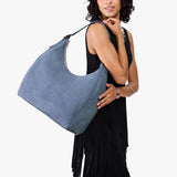 Denim Oversized | Model holding u-shaped, flat-bottomed leather shoulder bag with adjustable strap