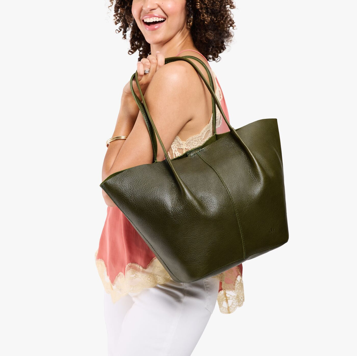 Model wearing sleeveless pink lace-trim top and white pants carrying an Oversized Devan Bucket Tote in Pebbled Olive