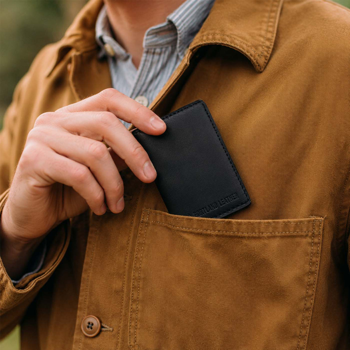 Nero | A close-up of a model sliding a leather card holder into their shirt pocket