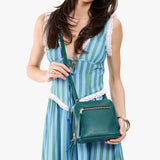 Sea Glass Small | Model holding compact leather bag with top zipper, front zipper pocket, and adjustable crossbody strap