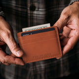 Toscano | A close-up lifestyle shot of a model holding a leather card holder with money and card inserted