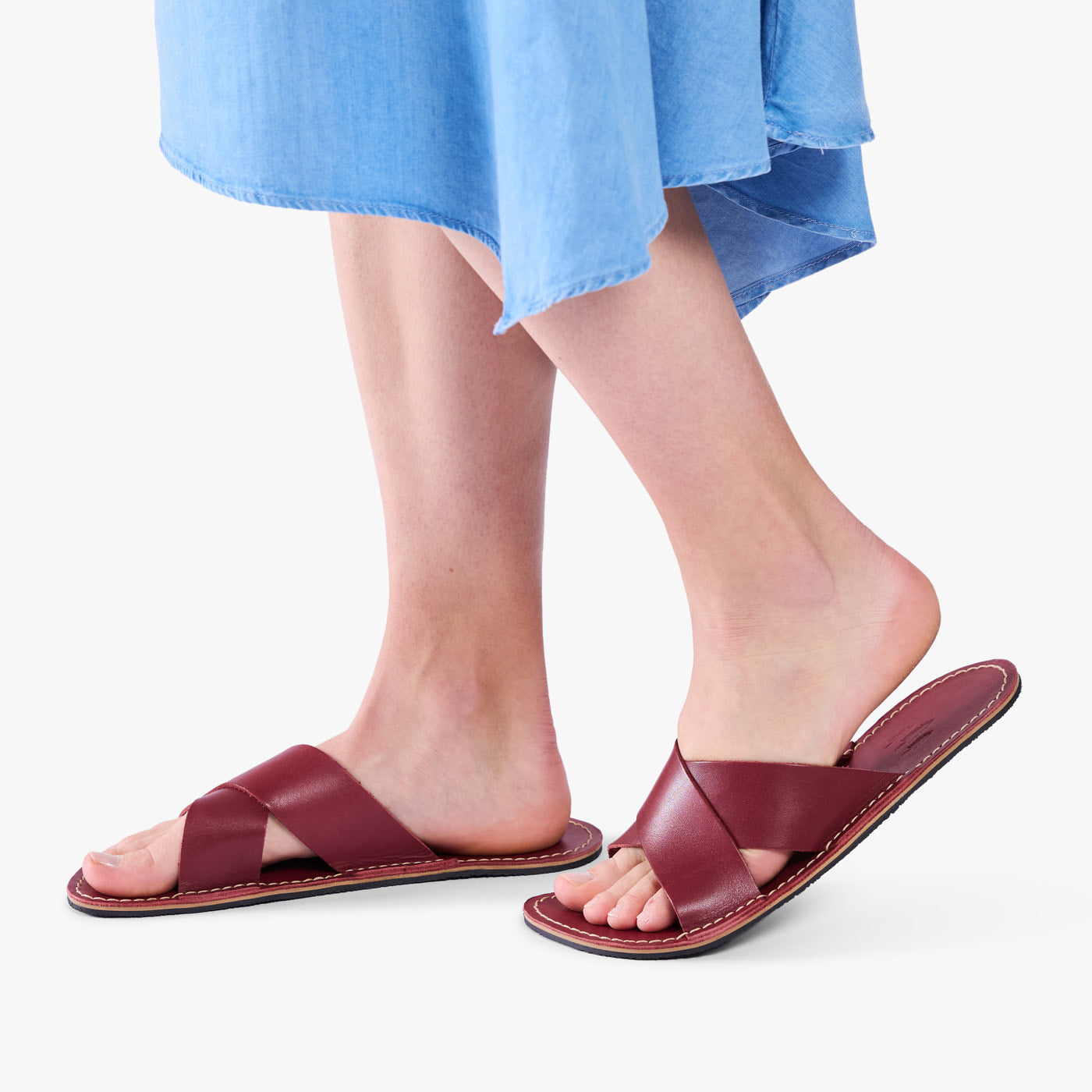 Marsala | Close-up of model wearing light blue dress and reddish brown flat sandals, shown against a plain background