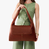 Nutmeg Large | A model holding a slouchy triangle shaped shoulder bag with a flap