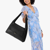 Pebbled--black Large | A model holding a slouchy triangle shaped shoulder bag with a flap