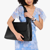 Pebbled--black Large | A model holding a slouchy triangle shaped shoulder bag with a flap