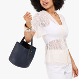 Night Owl Small | Model carrying symmetrical bucket bag with handle, latch closure, and removable crossbody strap