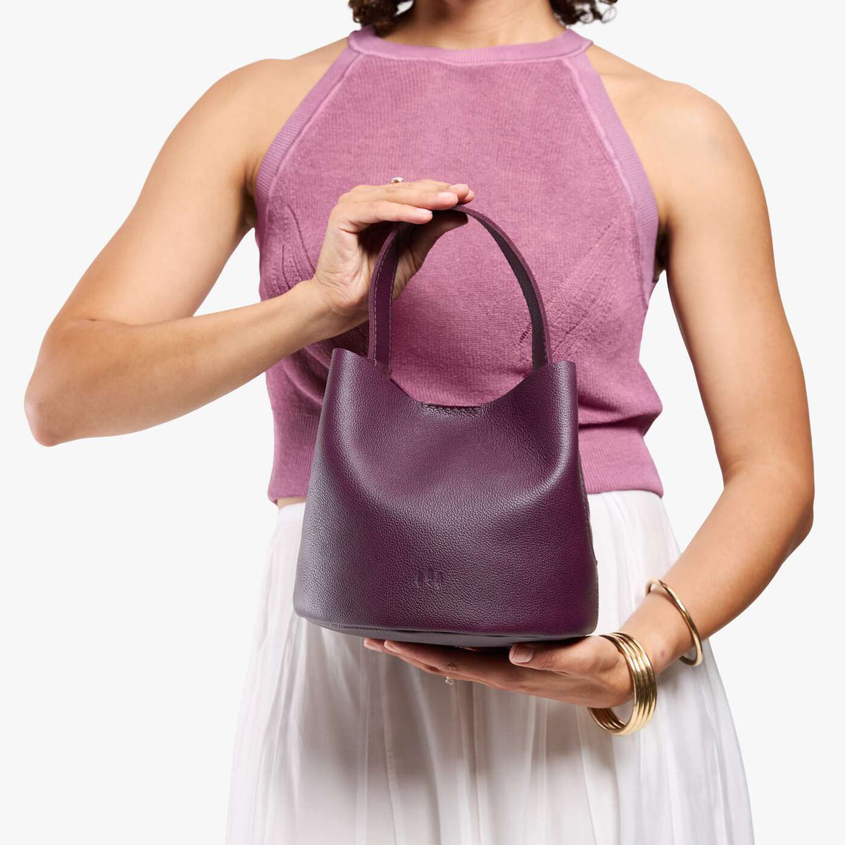 Plum*Small | Model holding symmetrical bucket bag with handle, latch closure, and removable crossbody strap