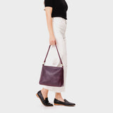 Plum Classic | Model holding leather triangular shoulder bag with zipper top closure and wide shoulder strap