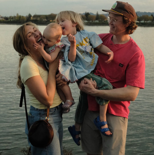 Family with two kids with mom and dad posing in front of a lake, with mom wearing a leather circle crossbody bag