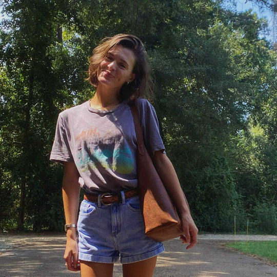 Woman wearing a brown leather shoulder bag in front of a forest background