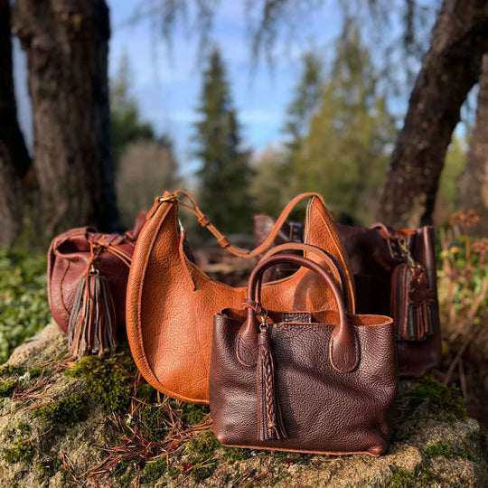 Collection of brown leather bags with leather tassel accessories in front of a forest background