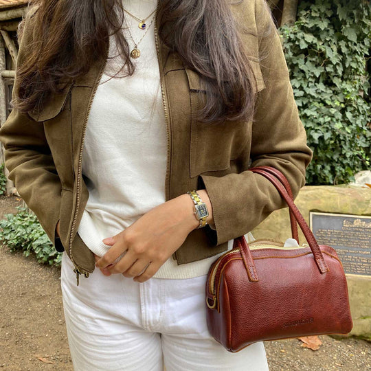 Women waring a watch and leather jacket carrying a brown leather handbag with zipper top