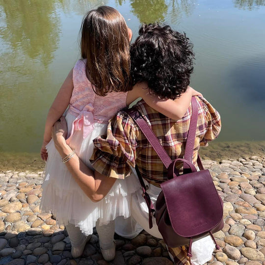 Mother wearing a purple leather backpack sitting in front of pond with child