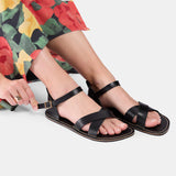 Nero | Close-up of model wearing floral-print dress and black flat sandals with an ankle strap and buckle, shown against a plain background