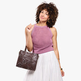Sepia | Model holding structured mid-size tote bag with overlapping panels and crossbody strap