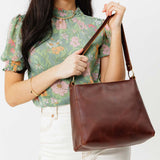 Cognac Classic | Model holding leather triangular shoulder bag with zipper top closure and wide shoulder strap